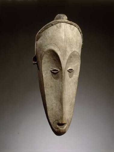 Central African mask in pale wood, with a very elongated face, almond-shaped eyes and an arched brow