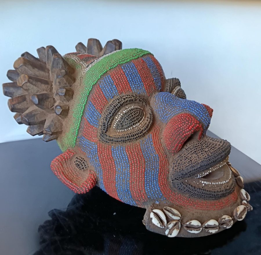 Cameroonian ceremonial object: a head covered in red, blue and green glass beads, adorned with cowries and a carved wooden crest